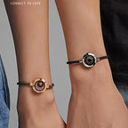 Two wrists wearing black cord bracelets with circular metal ends.